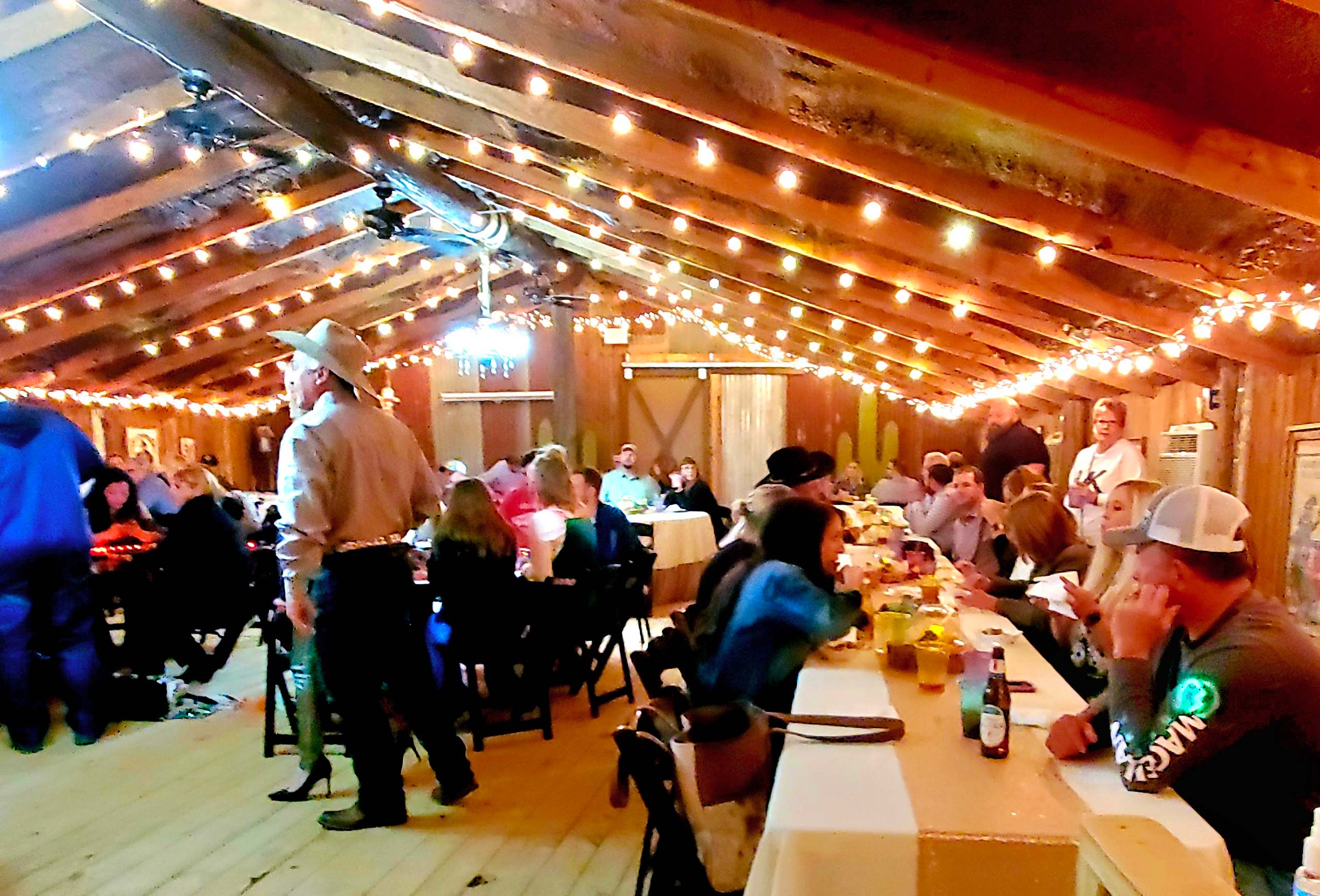 Guests celebrating inside the barn under string lights at Chisholm Trail Rustic Venue