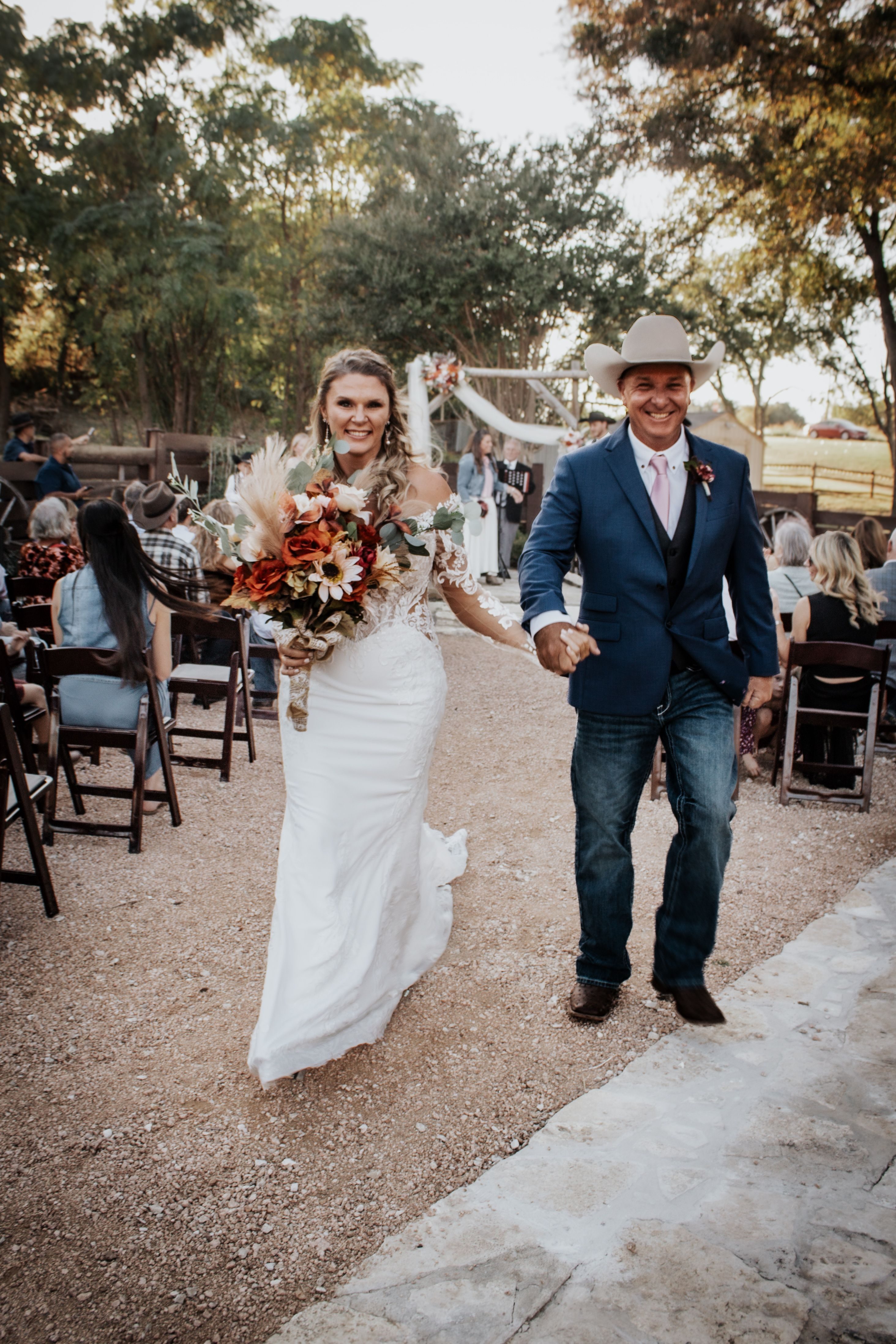 Newlywed couple walking from the outdoor ceremony area at Chisholm Trail Rustic Venue